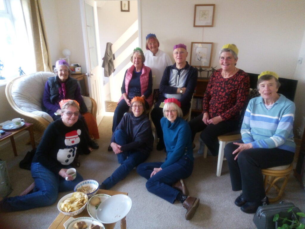 A group of 9 people sitting in a lounge with food and Christmas hats