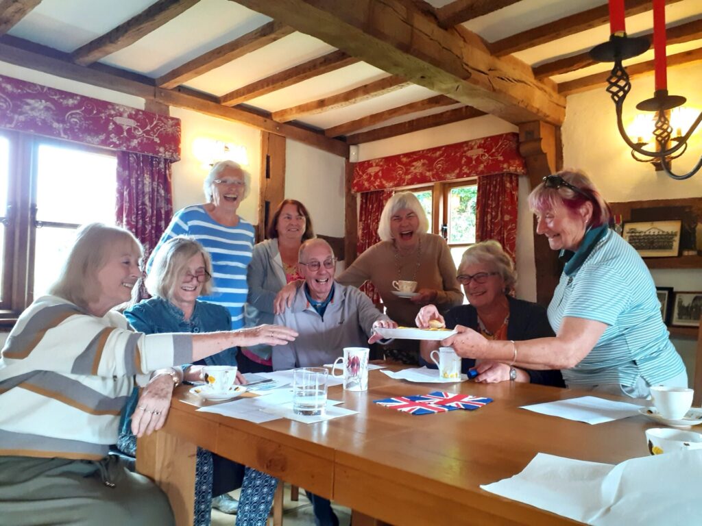 a group of 8 people round a table, smiling and reaching for cake