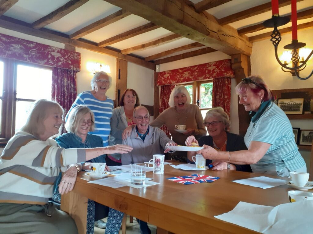 a group of 8 people around a table smiling and reaching for cake
