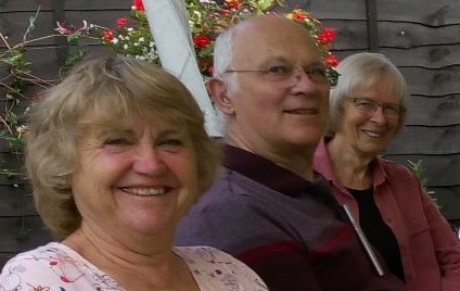 Three people smiling towards the camera with plants behind