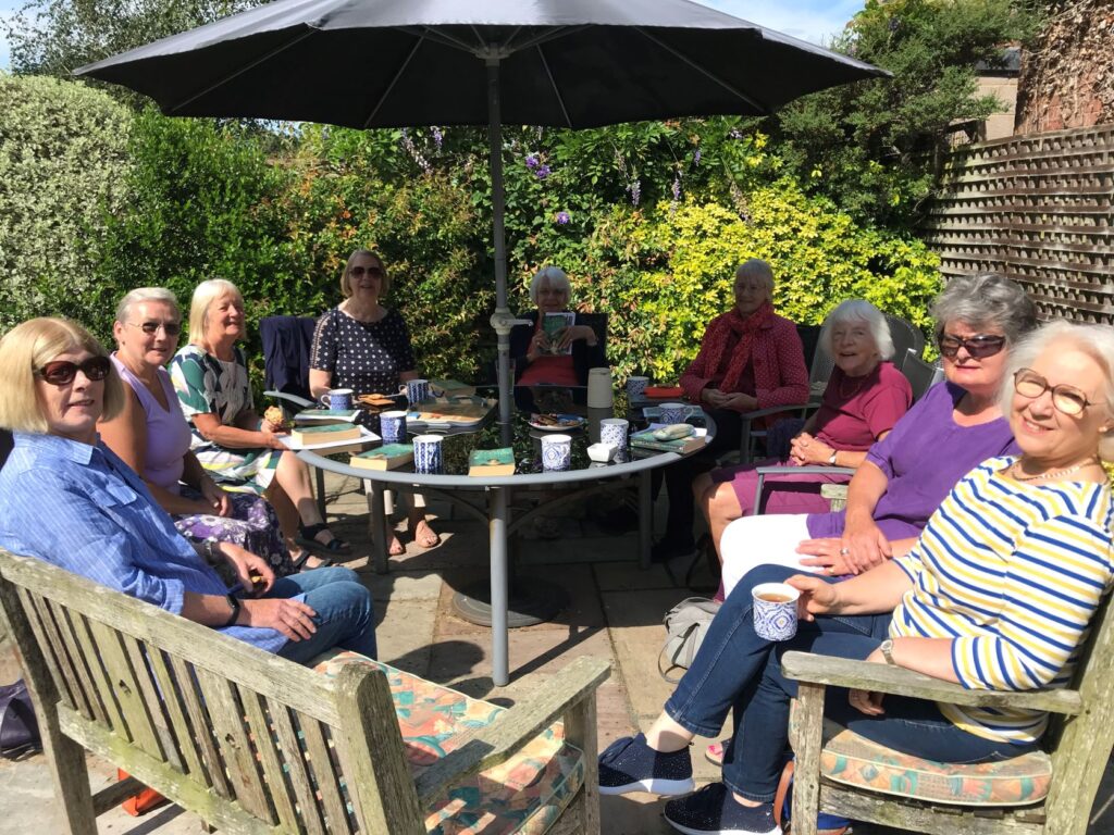 a group of 9 women around a table with a parasol in a sunny garden